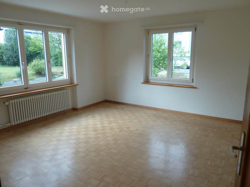 Empty room with wooden flooring, white walls, large windows, radiator, and wooden window sills.