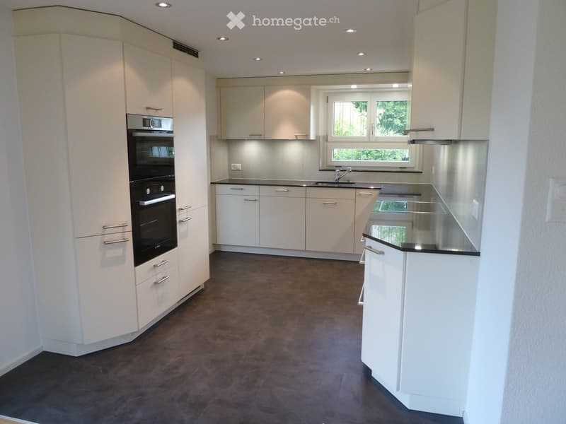 Modern kitchen with white cabinets, stainless steel appliances, and a large window offering a view of greenery.