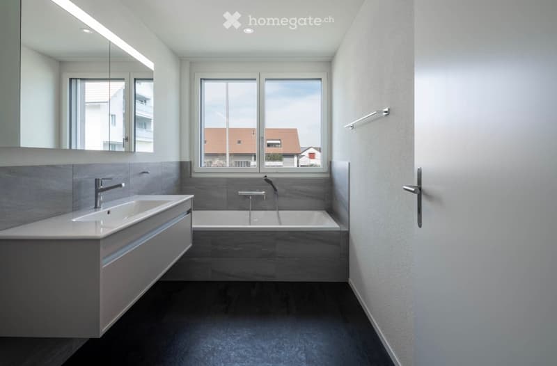 Modern bathroom with a white sink, bathtub, and large window offering a view of the neighborhood.