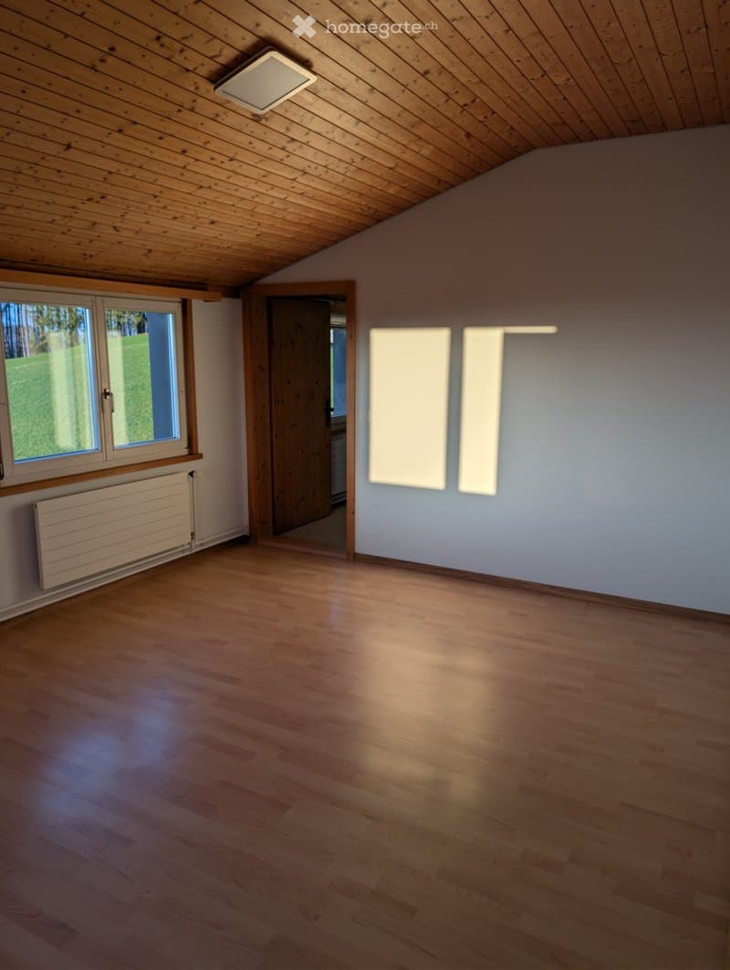 Empty room with wooden floor, white walls, large window, and a door leading to another room. No furniture or equipment present.