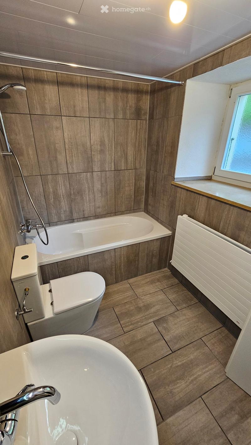 Modern bathroom with a bathtub, toilet, and a separate shower area. Features wooden tiled walls and a window with a small shelf.