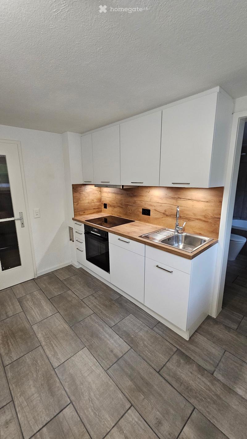 Modern kitchen with white cabinets, wooden countertop, stainless steel sink, and built-in oven. Features include a wooden backsplash and tiled flooring.