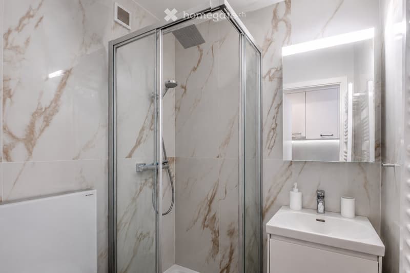 Modern bathroom with marble tiles, glass-enclosed shower, white sink, and mirror.