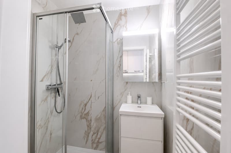 Modern bathroom with a glass-enclosed shower, marble tiles, a white sink with a mirror, and a white radiator.