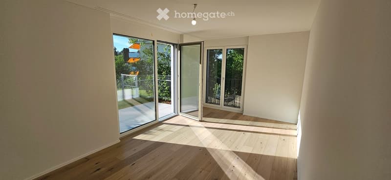 Empty room with wooden flooring, large sliding glass doors leading to an outdoor area, and natural light streaming in.