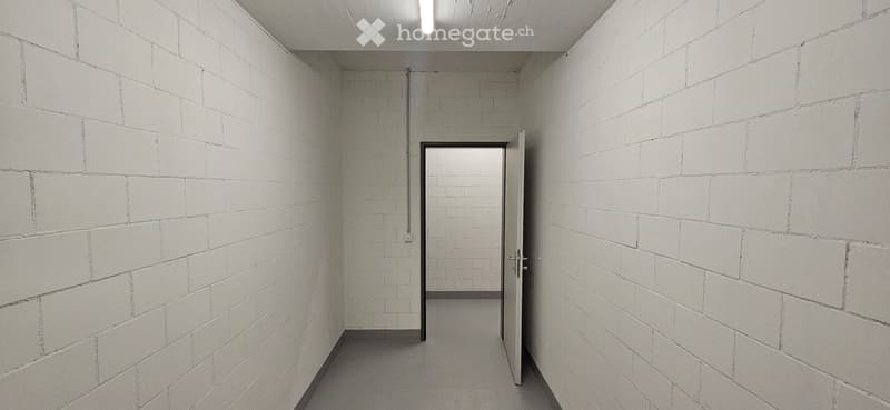 Empty hallway with white brick walls, a single open door leading to another room, and a visible electrical outlet on the wall.