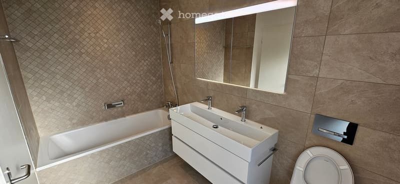Modern bathroom with a large bathtub, double sink, toilet, and a large mirror with LED lighting.
