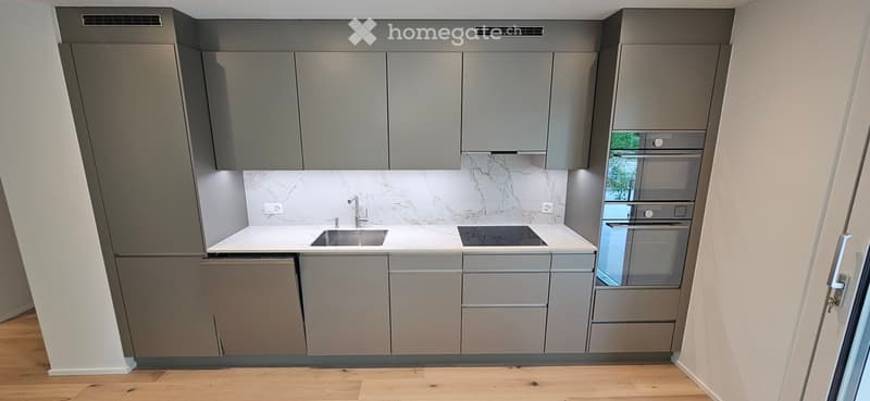 Modern kitchen with grey cabinets, white marble backsplash, stainless steel sink, stove, and built-in oven.