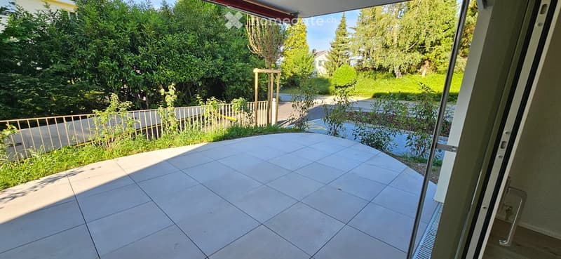 Balcony with tiled floor, metal railing, and view of a green garden and trees.