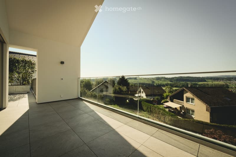 Modern balcony with large glass railing, tiled floor, and scenic countryside view.