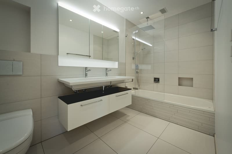 Modern bathroom with a double sink, large mirror, bathtub, toilet, and shower area with glass enclosure.