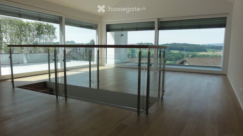 Empty room with wooden flooring, large glass windows, and a glass railing leading to a balcony or terrace.