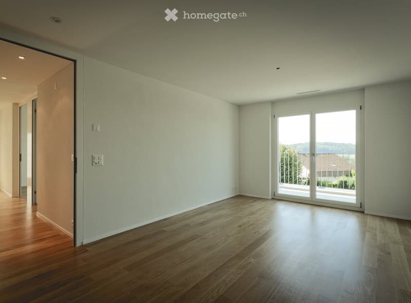 Empty room with light-colored walls and wooden flooring, featuring a large sliding glass door leading to a balcony.