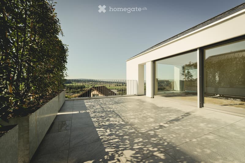 Modern balcony with large glass sliding doors, tiled floor, metal railing, and scenic countryside view.