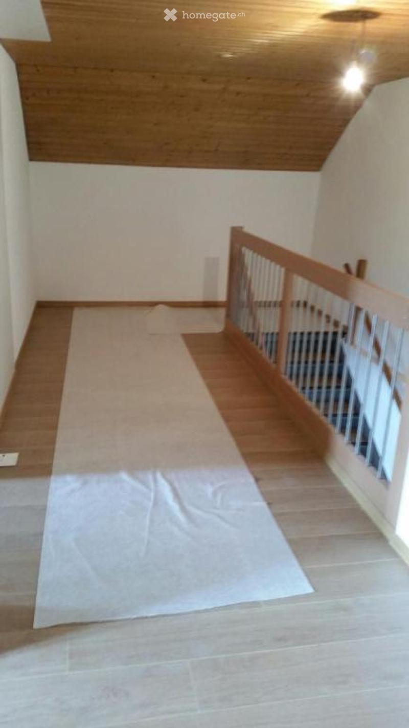 Empty room with wooden flooring and a wooden staircase railing, no furniture or equipment present.
