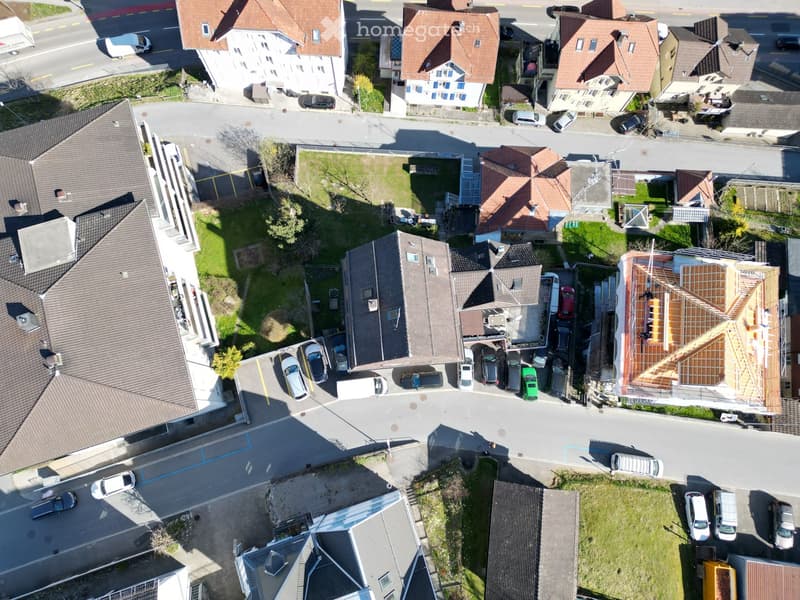 Aerial view of a residential neighborhood with multiple houses, parked cars, and a construction site with exposed wooden framing on one roof.