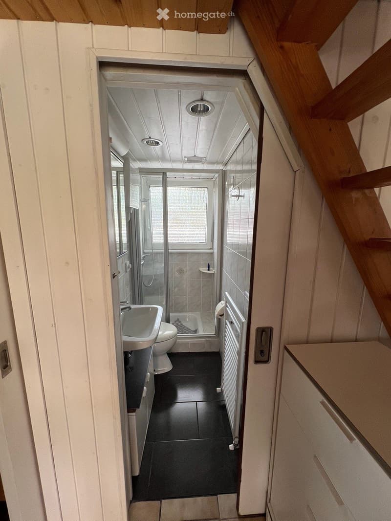 Modern bathroom with black tiled floor, white walls, a sink, toilet, bathtub, and a glass-enclosed shower area. The space features a radiator and a window above the bathtub.