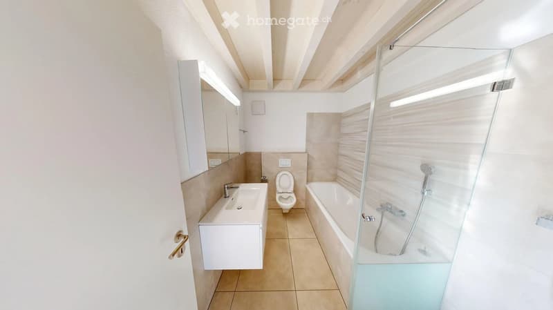 Modern bathroom with a white sink, toilet, bathtub, and glass-enclosed shower. Light-colored tiles and a sleek design.