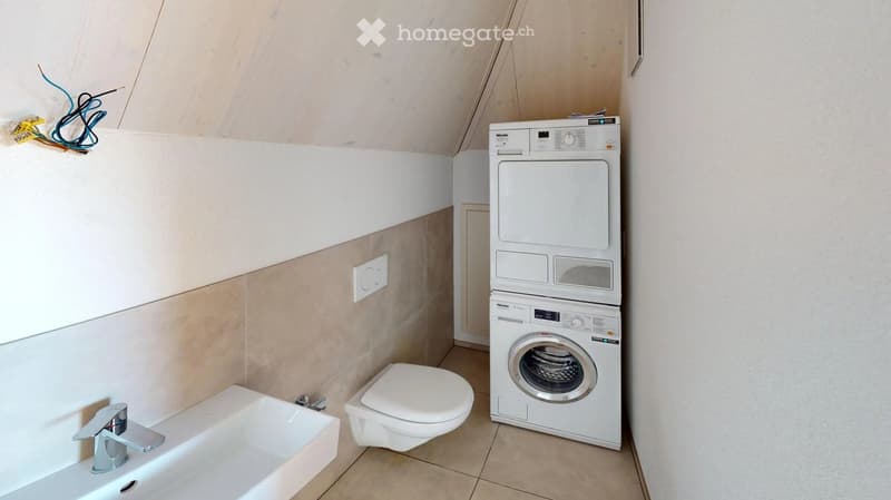 Modern bathroom with a white sink, chrome faucet, toilet, and stacked white washing machine and dryer unit.