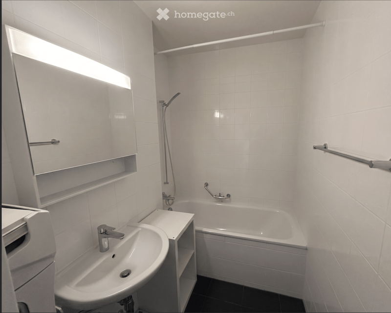 Modern bathroom with white tiles, a sink, bathtub, mirror, and showerhead.