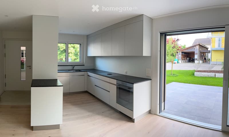 Modern kitchen with white cabinets, black countertops, and a large sliding glass door leading to a patio and garden.