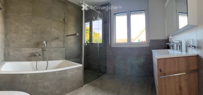 Modern bathroom with a bathtub, glass-enclosed shower, wooden sink cabinet, and large windows providing natural light.