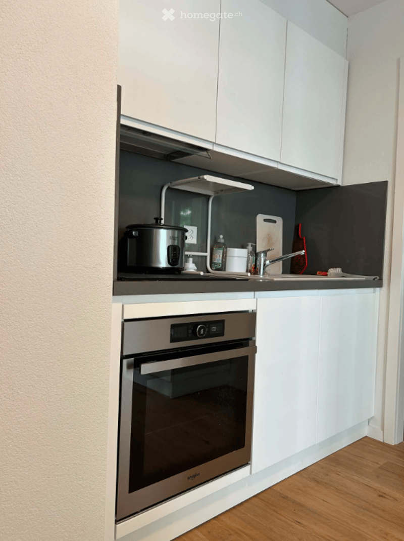 Modern kitchen with white cabinets, stainless steel oven, countertop, and various kitchen items including a cooker, faucet, and cutting board.