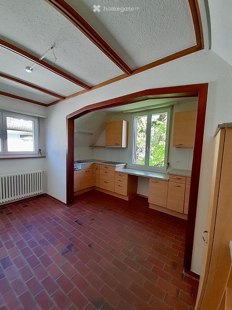 Empty kitchen with wooden cabinets, a sink, and a radiator, featuring a red tiled floor and white walls.