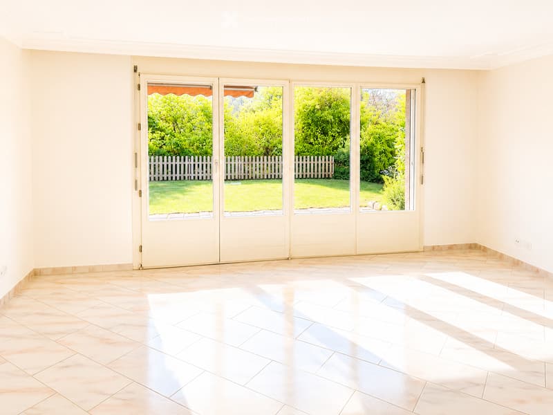 Empty room with light-colored tiled flooring and large sliding glass doors leading to a garden area.