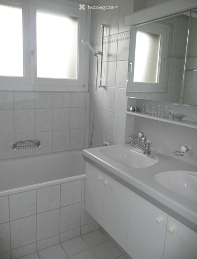 Modern bathroom with a bathtub, double sink, mirror, and shower. The space features white tiles and a clean, contemporary design.