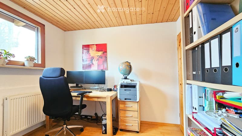 A well-organized home office with a wooden desk, ergonomic chair, dual monitors, printer, globe, bookshelf with file folders, and decorative painting.