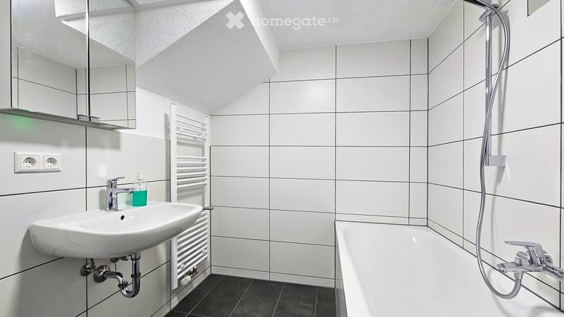 Modern bathroom with white tiles, a sink, a bathtub, a mirror, a radiator, and a bottle on the sink.