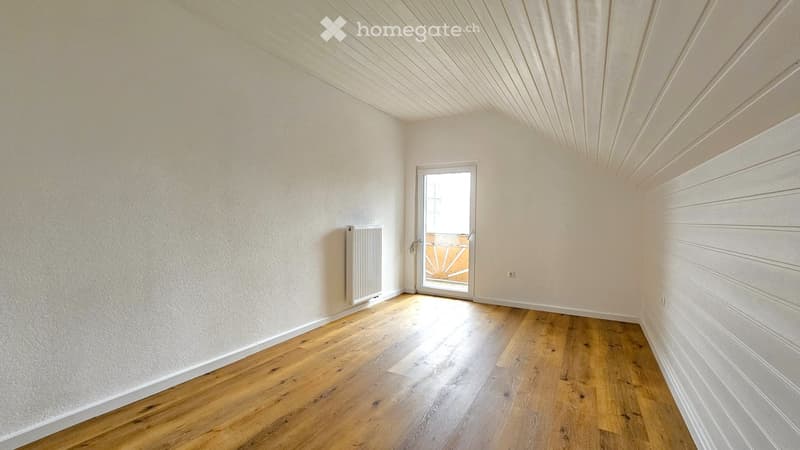 Empty room with wooden flooring, white walls, and a white radiator. A sliding glass door leads to a balcony or outdoor area.