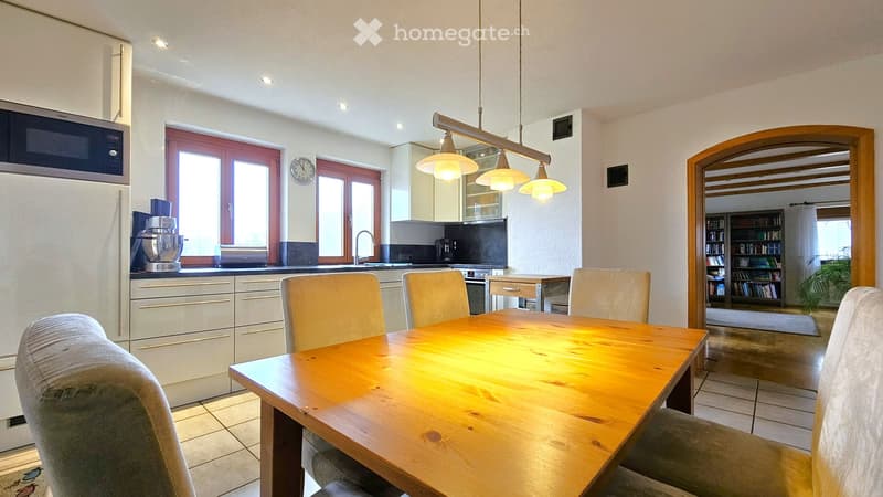 Bright, modern kitchen with white cabinets, stainless steel appliances, a wooden dining table with six chairs, and a large window providing natural light.