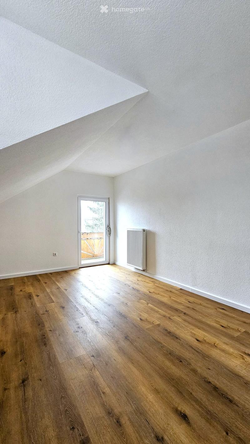 Empty room with wooden flooring, white walls, and a radiator. A sliding glass door leads to an outdoor area.