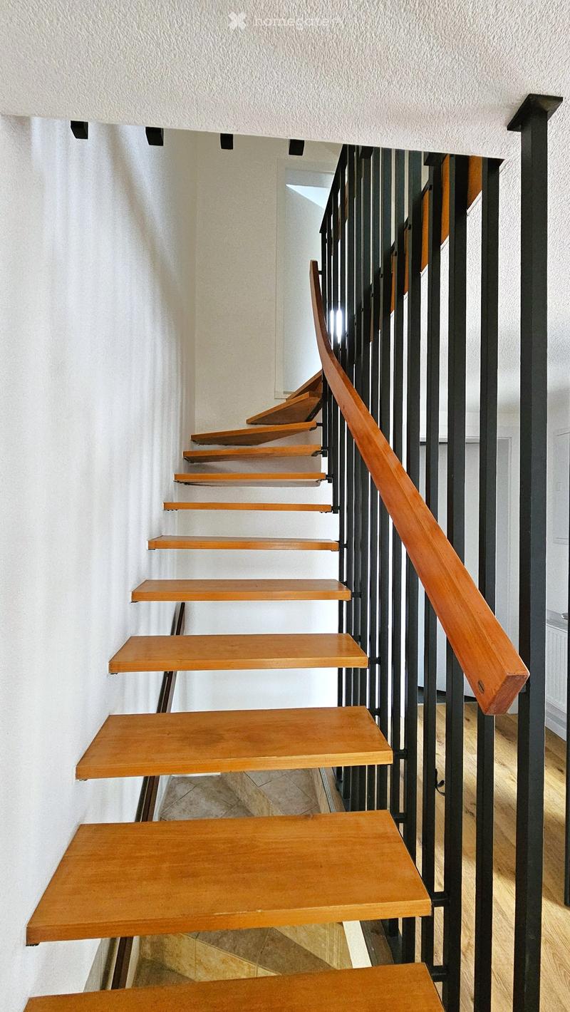 Wooden staircase with black metal railing, leading upwards, with wooden steps and a polished wooden handrail.