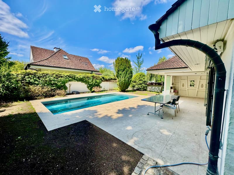 Outdoor area with a swimming pool, patio furniture, and surrounding greenery.