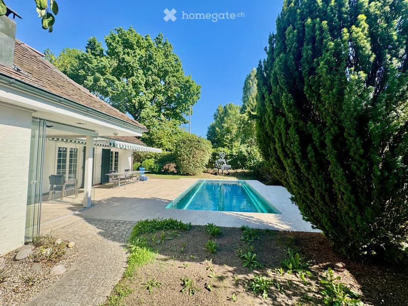 Outdoor area with a swimming pool, patio furniture, and surrounding greenery.