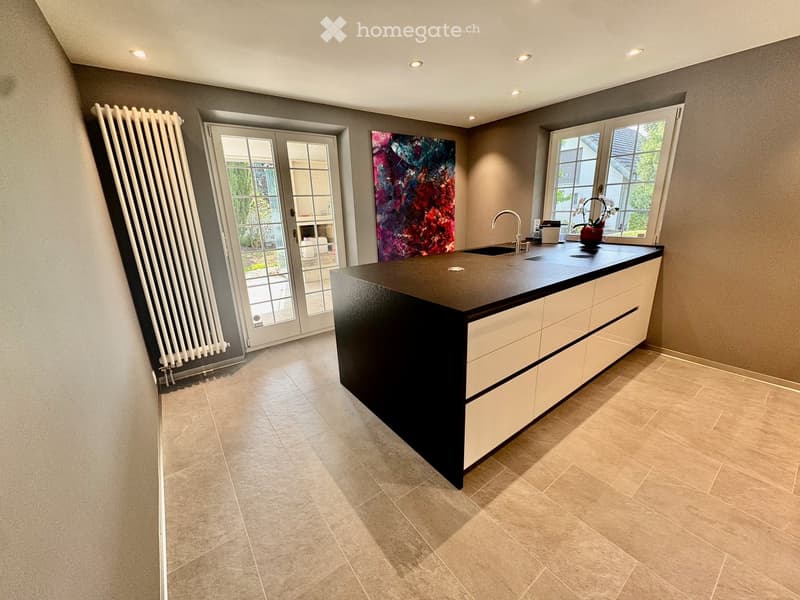 Modern kitchen with a central island, sleek black countertop, white cabinets, and a large window overlooking the garden.