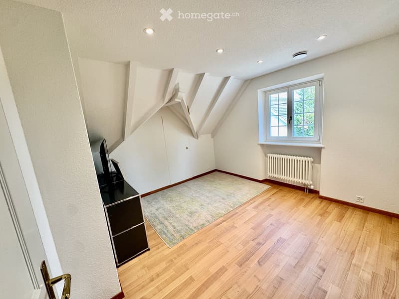 Empty attic room with wooden flooring, white walls, skylight windows, and a radiator. No furniture or personal items present.