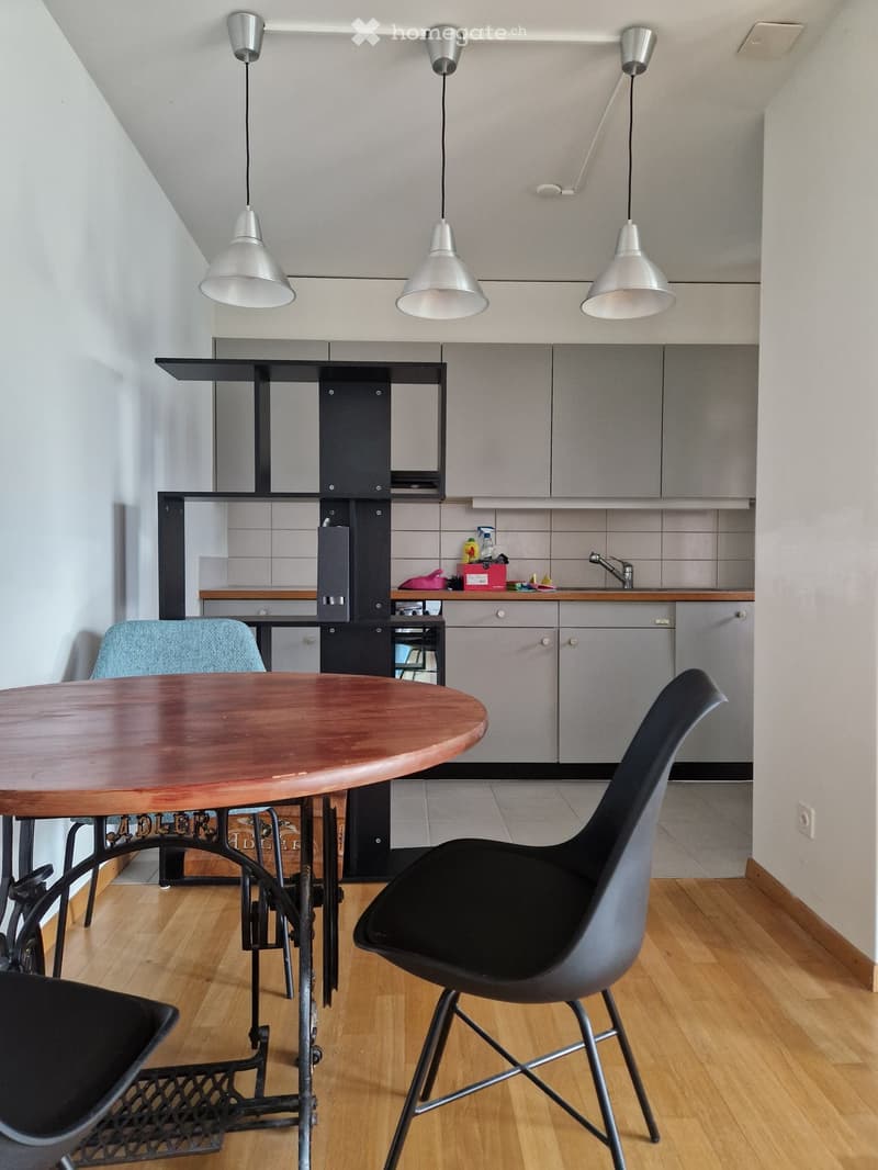 Modern kitchen with grey cabinets, wooden floor, round wooden table, black chairs, and pendant lights.