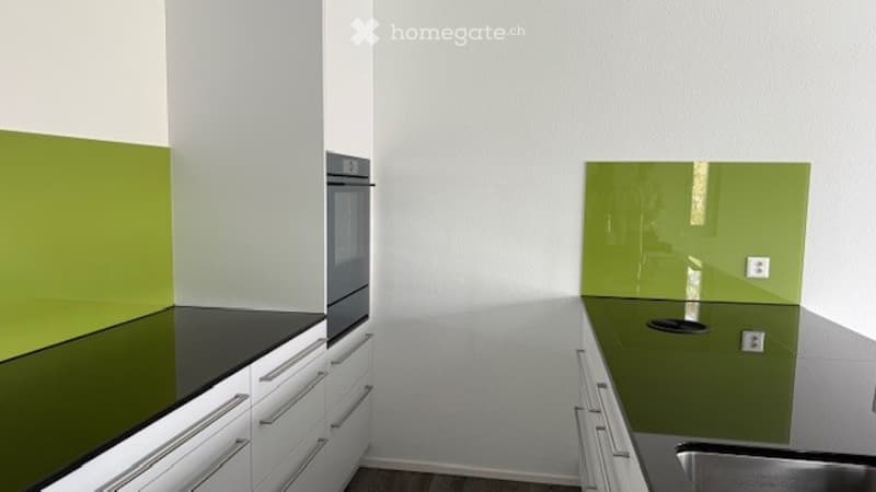 Kitchen. Modern kitchen with white cabinets, black countertops, and green backsplash accents. Features an oven and a sink.