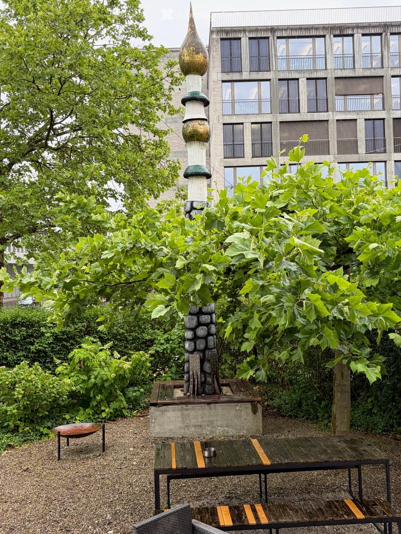 Garden area with a wooden table, chairs, a decorative stone structure, and lush greenery.