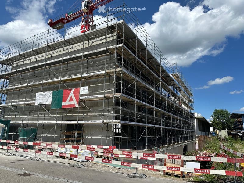 A multi-story building under construction, covered in scaffolding with visible construction materials and signage.
