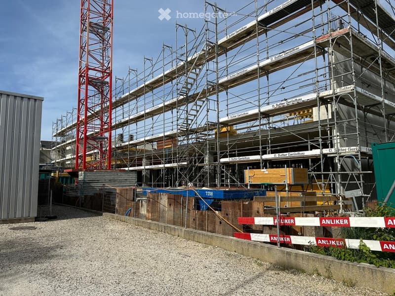 Multi-story building under construction with scaffolding, wooden planks, and construction materials visible.