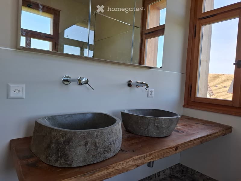 Modern bathroom with two stone sinks on a wooden countertop, chrome faucets, and a large mirror above.