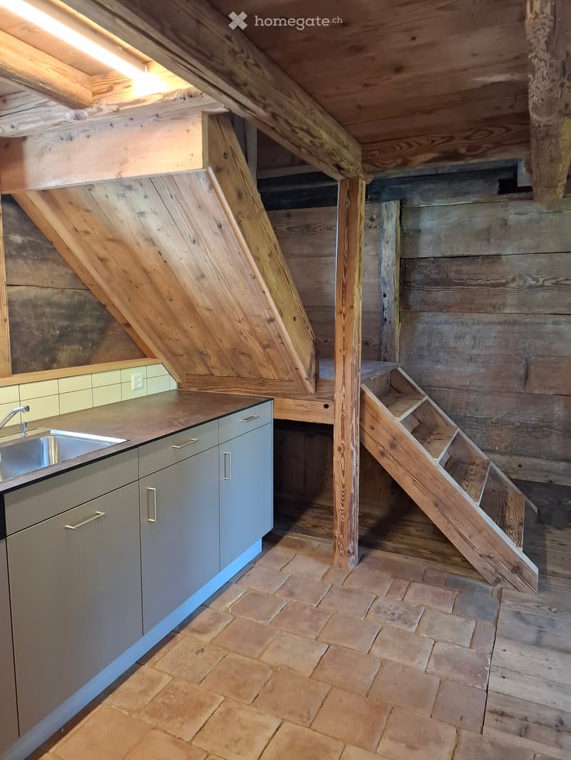 Modern kitchen with grey cabinets, stainless steel sink, and a wooden staircase leading to an attic space.