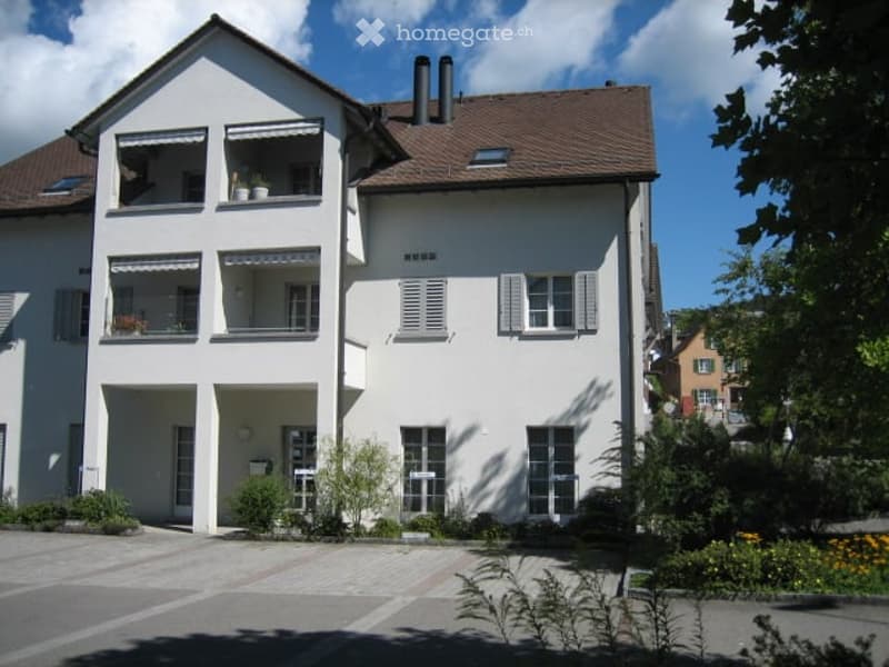 Two-story white house with multiple windows, balconies, and a well-maintained garden.