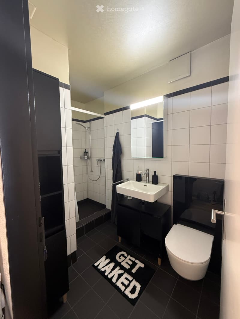 Modern bathroom with white tiles, black accents, a white sink, toilet, mirror, and a shower area with a glass door.