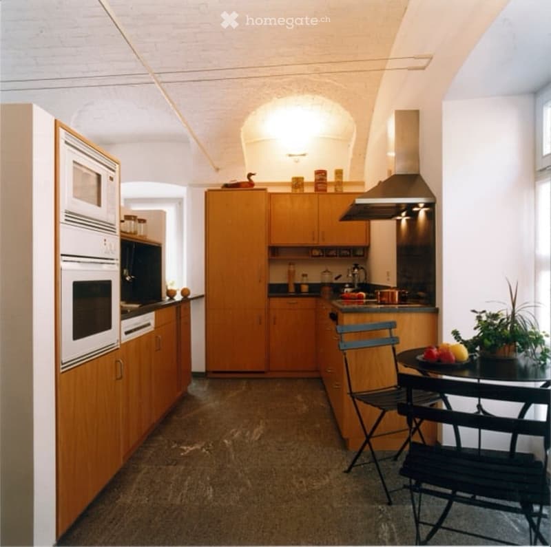 Modern kitchen with wooden cabinets, stainless steel appliances, a microwave, oven, stove, and a small dining area with a table and chairs.